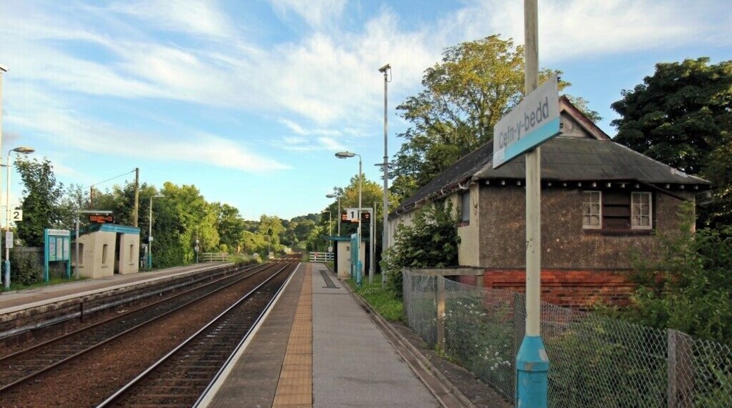 A railway station platform with tracks, a small building, and a signboard.