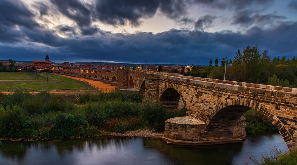 Arched medieval stone bridge Paso Honroso crossing the Orbigo River at dusk. Historic landmark in Hospital de Orbigo, Leon, Spain, along the Camino de Santiago pilgrimage route.