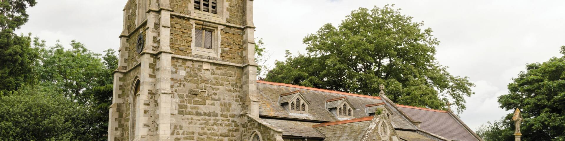 There is no mention of the church in the Domesday book, but there are indications that the first building was early Norman. The church is first documented in 1280. The church is constructed with greenstone with brickwork and ashlar dressings. The roof is slate. There is a western tower, nave with south aisle, chancel, vestry, and south porch. The tower is of three stages dating from the 15th century, it was largely rebuilt in the 19th century. It has a plain parapet and crocketted pinnacles. There is a date stone of 1684 on a plaque which marks the rebuilding of the tower which had collapsed. On the second stage of the tower there is another date stone of 1894 from when the upper part was rebuilt. There a three bay south arcade with octagonal piers from the 15th century. The nave also has three 19th-century dormer windows on the south side which were in inserted in 1911. The chancel was rebuilt in 1870 by James Fowler, the 15th century chancel arch being retained. There is a modern rood loft and screen, the original rood stairs are still present. Either side of the rood are two wooden carved Angels, probably dating from the 15th century and taken from Louth church. In the 19th century porch there is a Norman holy water stoup. There is a 14th century octagonal font set on a Minton tile dias. In 1877 the church underwent major restoration which included new roofs, porch, installation of heating, new floors plus other improvements. This was not finished until 1894 due to financial issues.