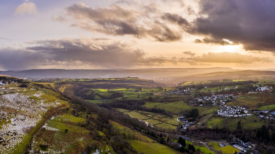 A valley with scattered houses, rolling hills, and a cloudy sky.