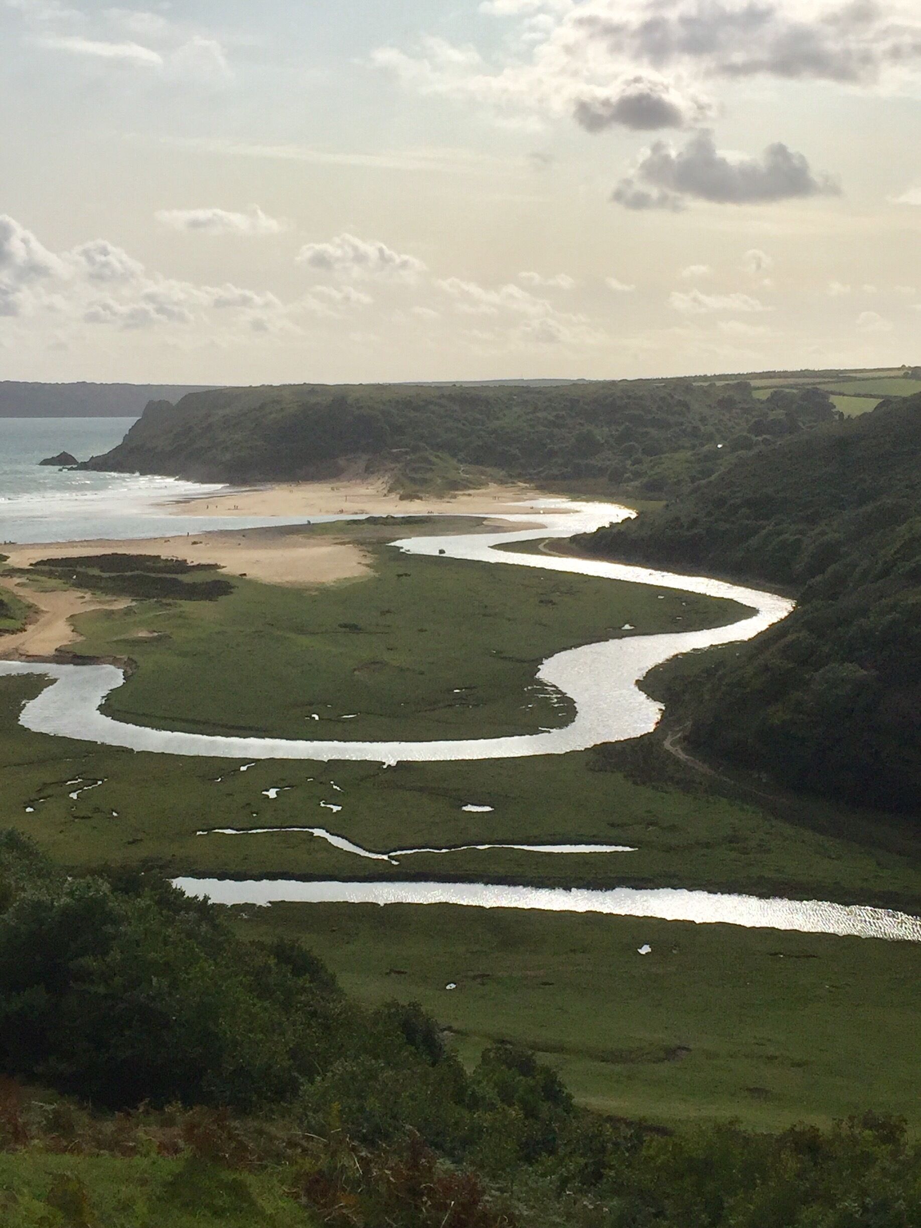 A river winding through a coastal landscape with a beach and cliffs.