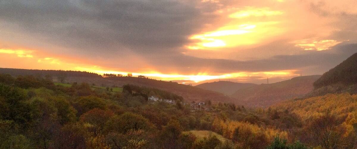 A valley with autumn foliage, a river, and distant hills under a sunset sky.