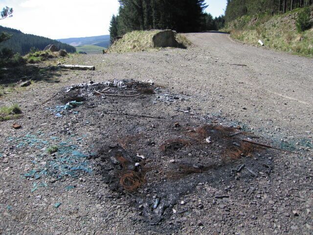 Burnt out Right at the edge of the square, the weird remnant of a burned-out car. Each side window is obvious as blue shards. Someone seems to have taken all the large metal bits, and the front bumper - away from the camera - has been reduced to white fibre.