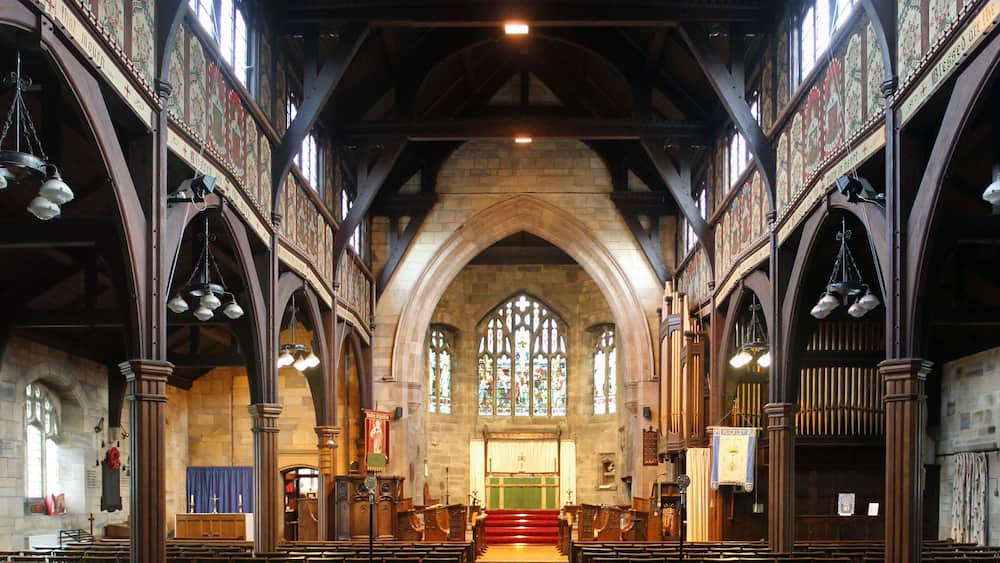 An interior of a church with wooden pews, stained glass windows, and a high arched ceiling.