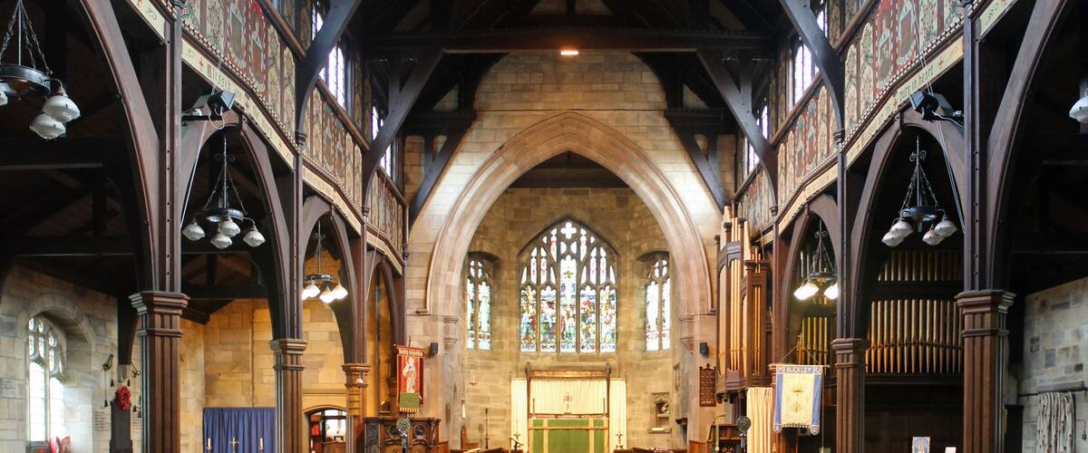 An interior of a church with wooden pews, stained glass windows, and a high arched ceiling.