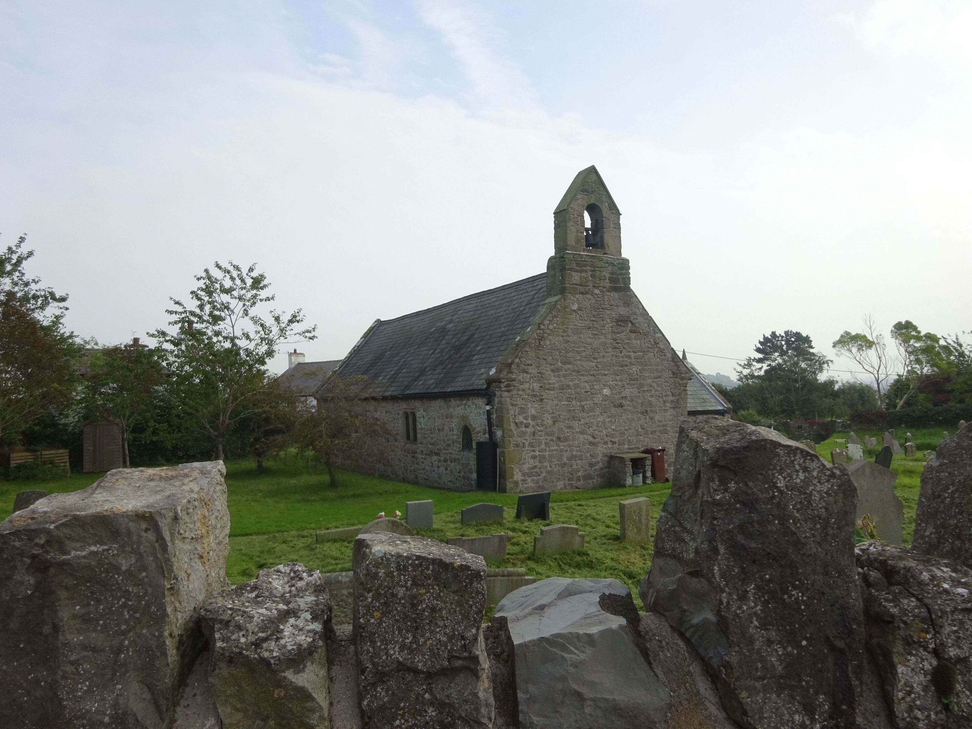 A stone church with a bell tower, surrounded by a cemetery with headstones.