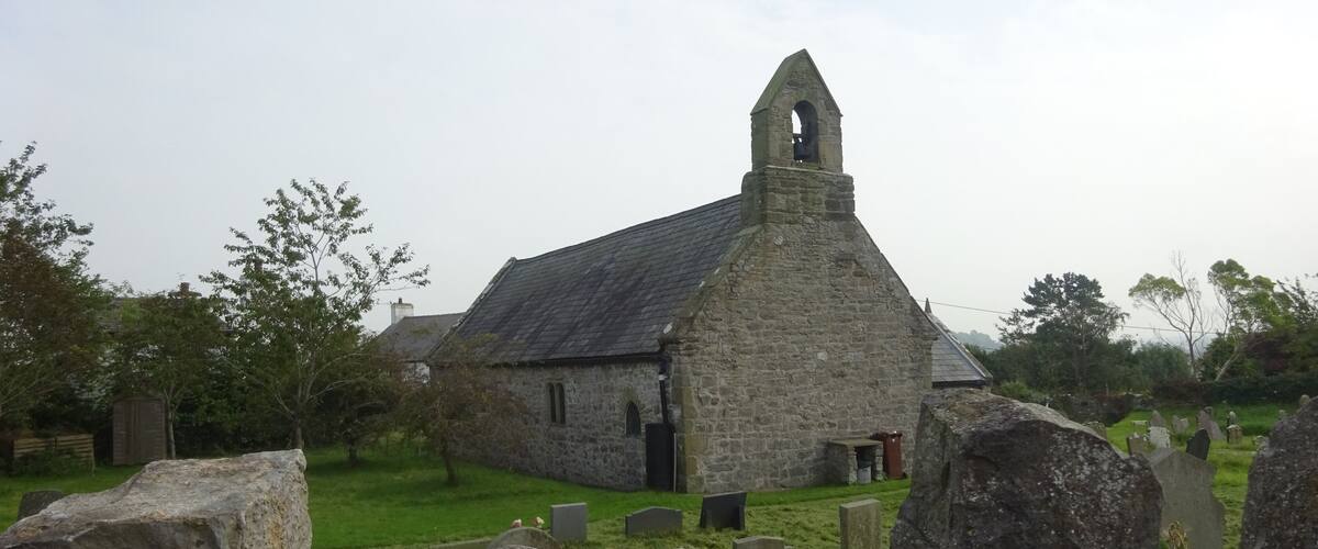 A stone church with a bell tower, surrounded by a cemetery with headstones.