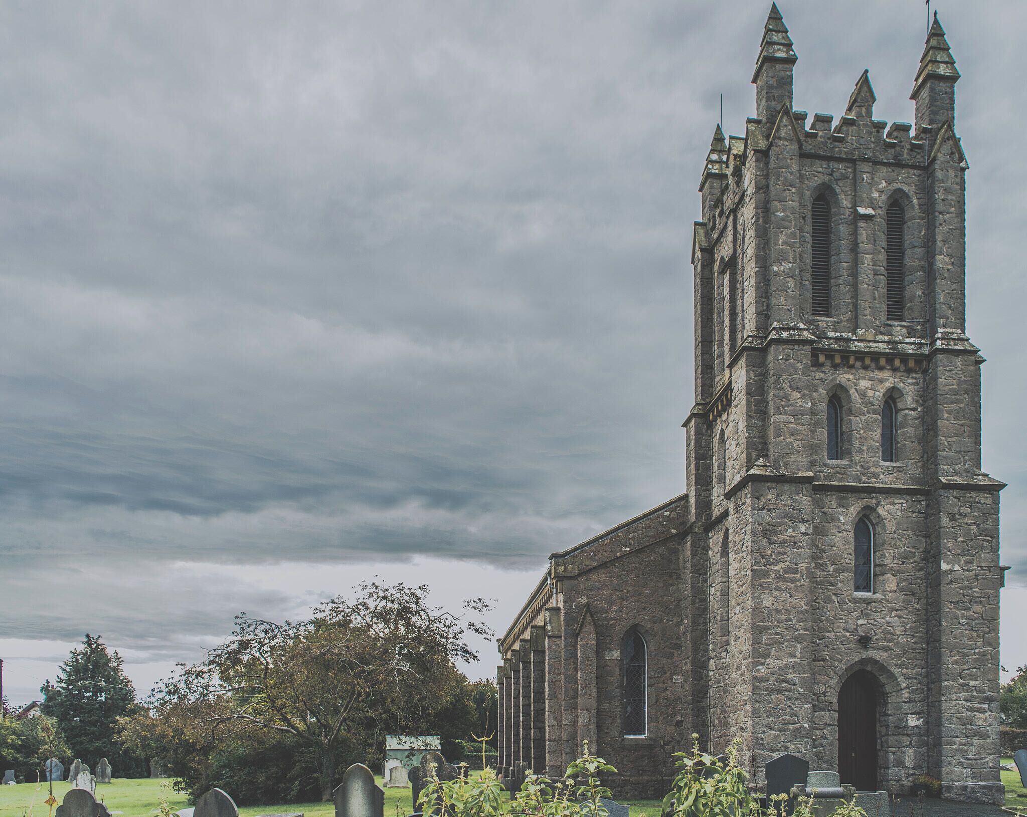 A historic stone church with a tall tower and arched windows, surrounded by a cemetery.