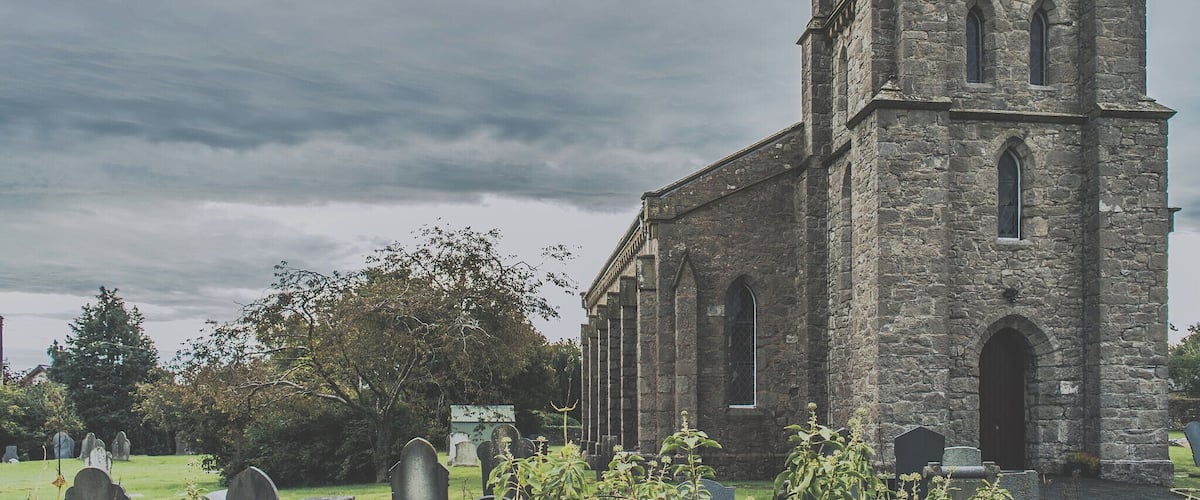 A historic stone church with a tall tower and arched windows, surrounded by a cemetery.