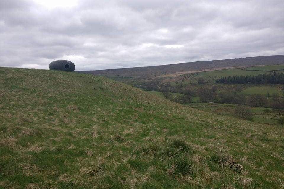 Une grande structure sphérique se dresse sur une colline verdoyante, avec une vallée en arrière-plan.