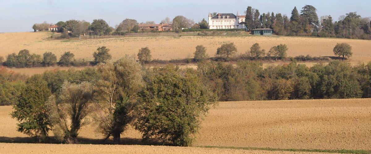 A rural landscape with rolling hills, scattered trees, and a large white house with a red roof on a hill.