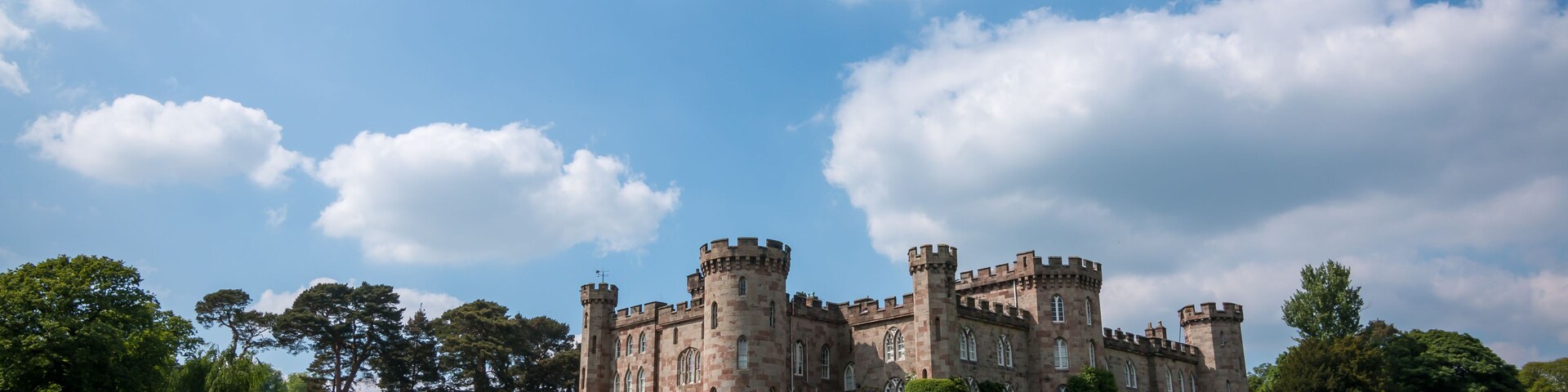 A historic castle with multiple towers and a well-maintained lawn in front.