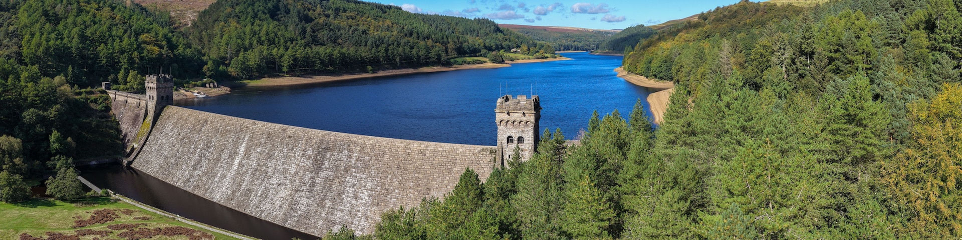 Una gran represa con una torre, rodeada de un bosque denso y un lago azul cristalino.