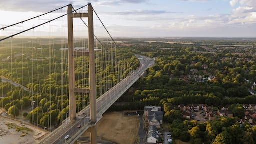 A large suspension bridge spanning a river, surrounded by lush greenery and residential areas.