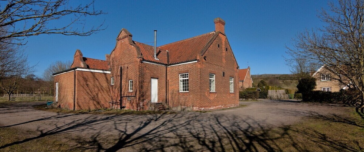 A large brick building with a steeply pitched roof, surrounded by a grassy area and trees.