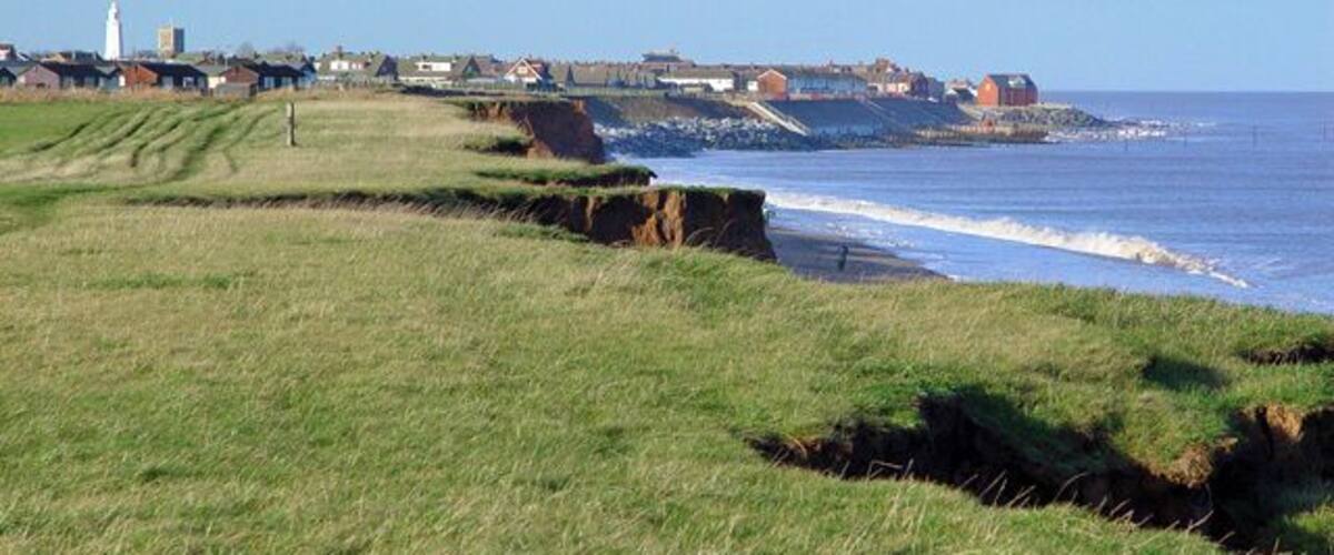 A coastal landscape with grassy fields, cliffs, and a lighthouse in the distance.