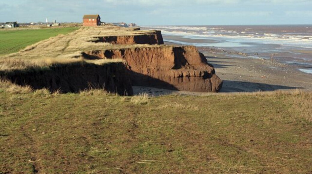 Coastal erosion south of Intack farm, Hollym, East Riding of Yorkshire, England. From this distance the farm building looks fine, but in fact the sea will remove the clay cliff in the fullness of time. The lighthouse and church in Withernsea are visible. The ability of the elements to take huge bites is clear from the photograph. See http://www.hull.ac.uk/coastalobs/general/erosionandflooding/erosion.html for the Hull University web page on coastal erosion including links to data and reports.