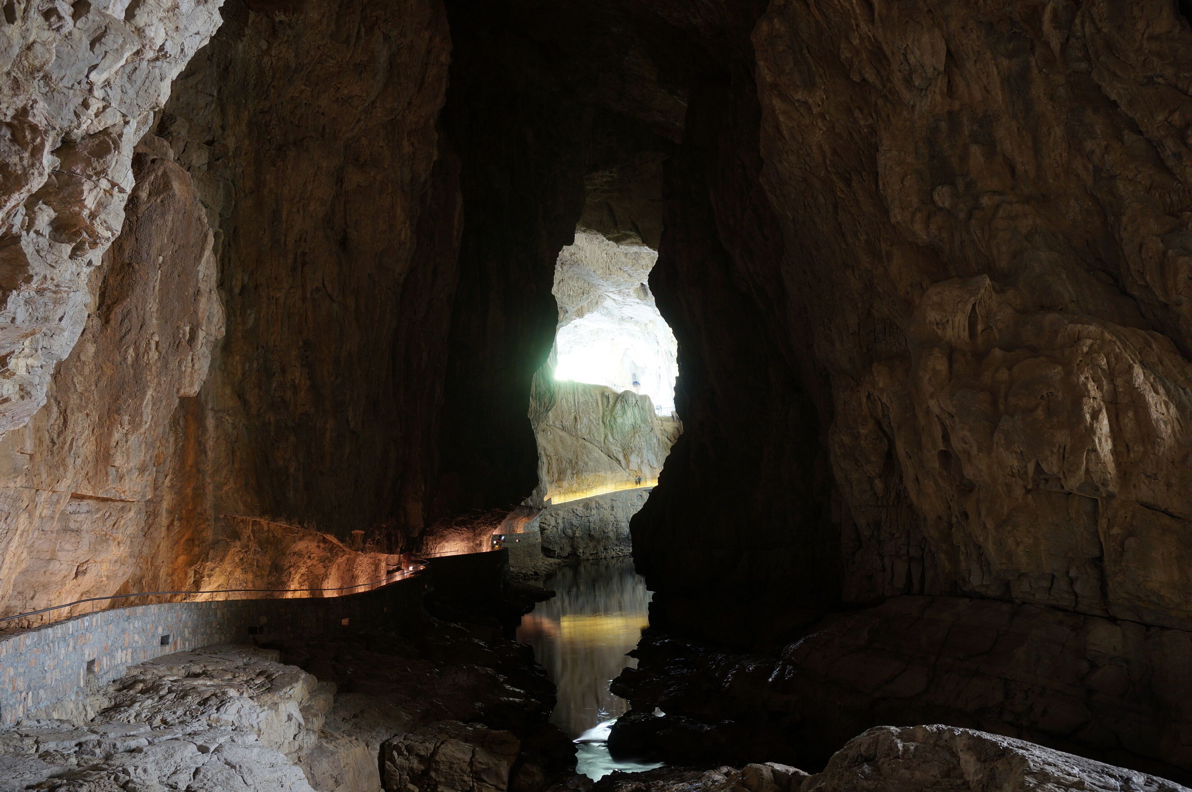 A cave with a water stream and a light source at the top.
