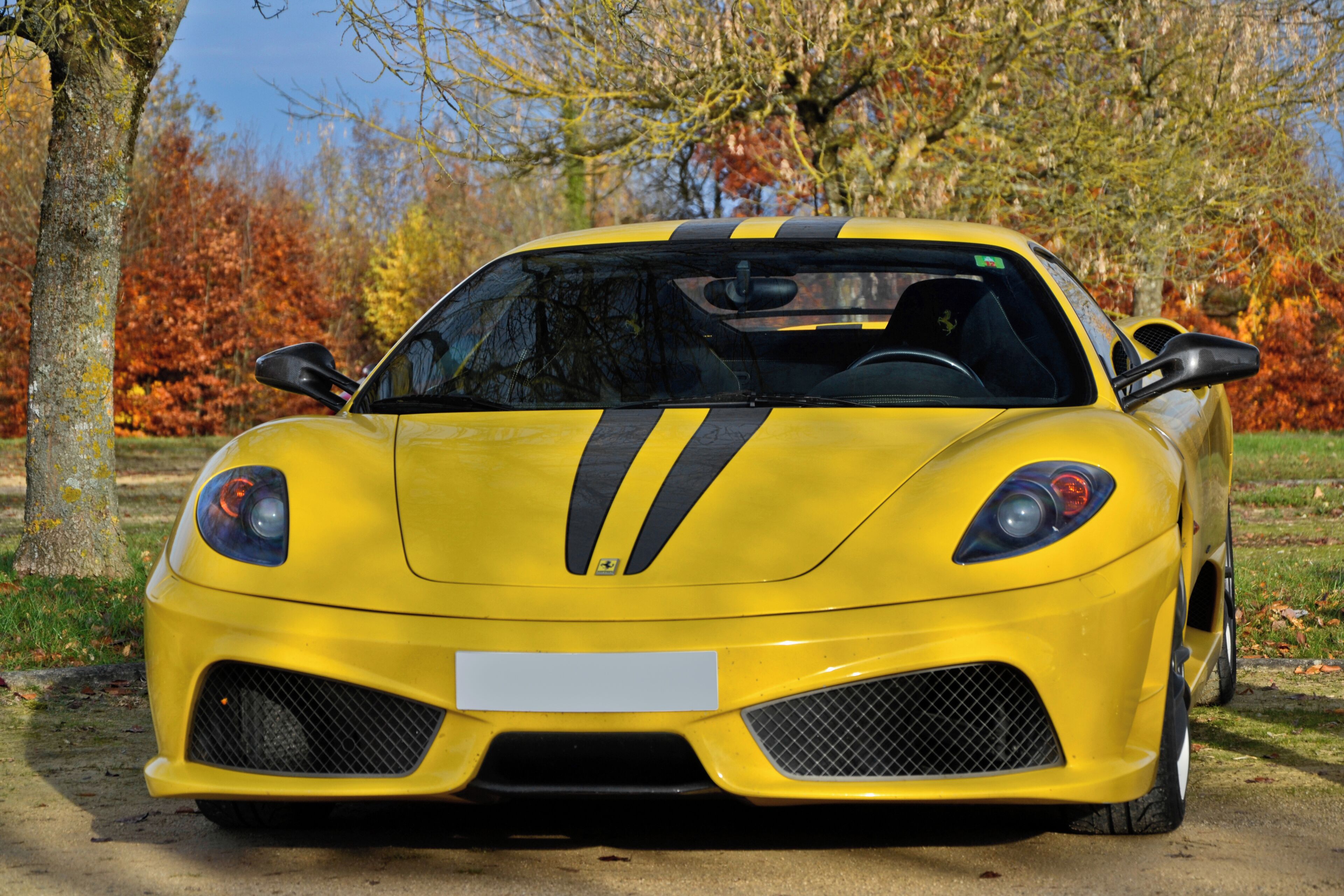 A yellow sports car parked on a concrete path with autumn trees in the background.