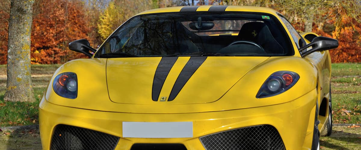 A yellow sports car parked on a concrete path with autumn trees in the background.