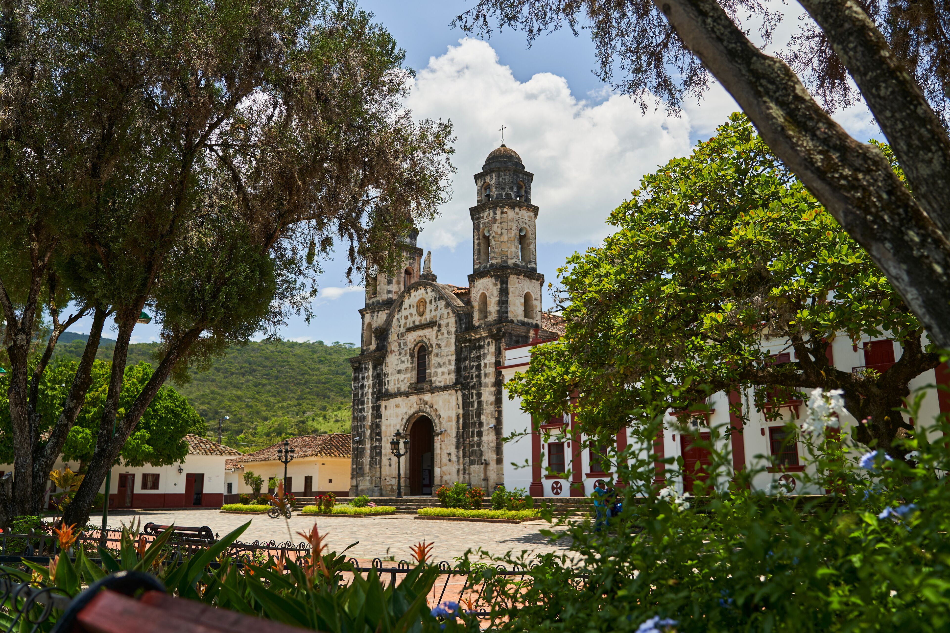 A historic church with two bell towers, surrounded by lush greenery and a cobblestone plaza.