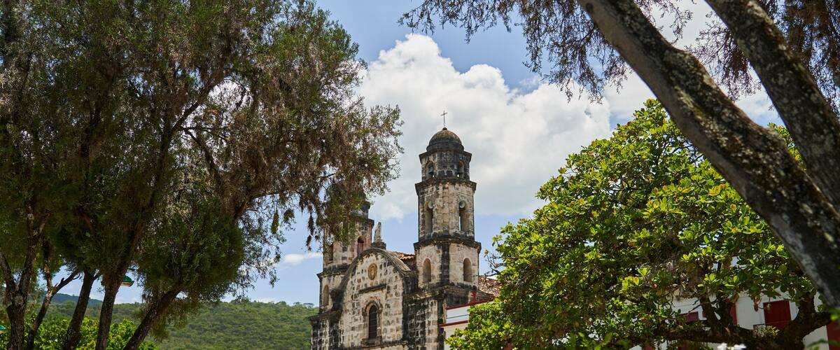 A historic church with two bell towers, surrounded by lush greenery and a cobblestone plaza.