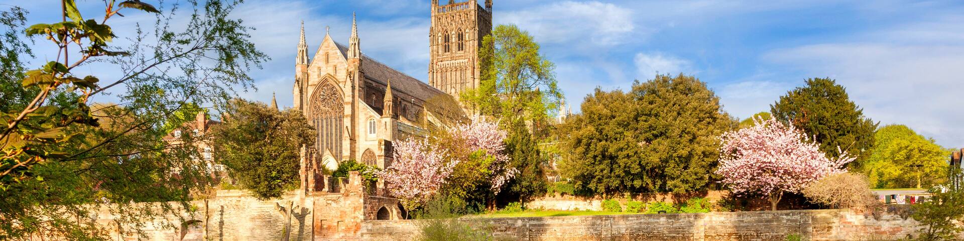 A historic cathedral with a large rose garden and a calm river reflecting its architecture.
