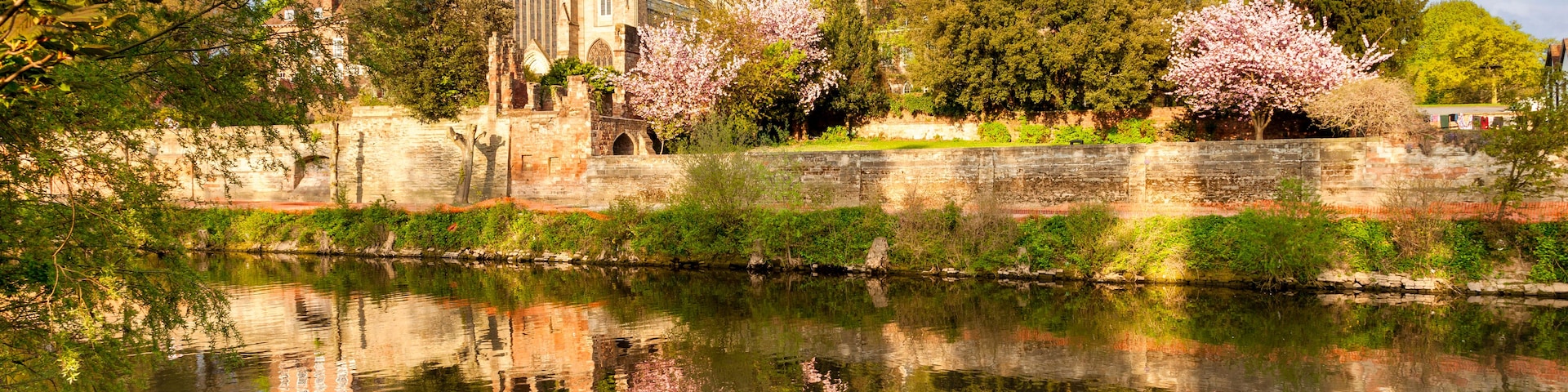 A historic cathedral with a large rose garden and a calm river reflecting its architecture.
