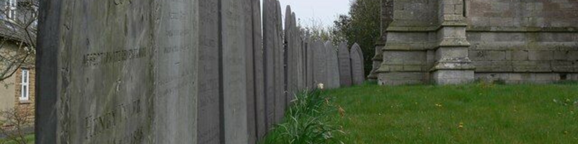 Filas de lápidas en un cementerio con un edificio de piedra al fondo.