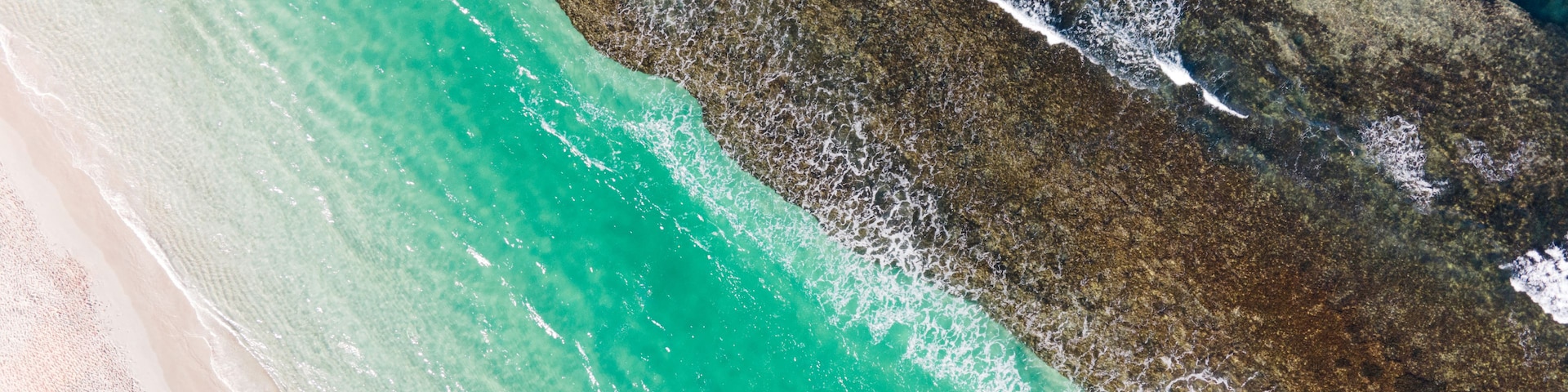 Une plage à l’eau turquoise et limpide, bordée d’un rivage de sable blanc et ponctuée de formations rocheuses.