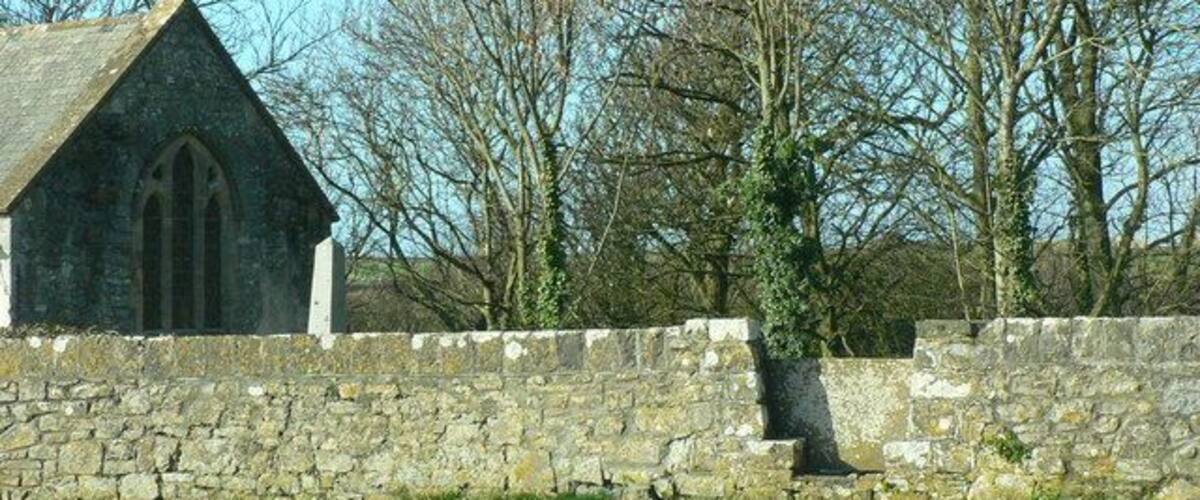 A stone church with a pointed roof and arched windows, surrounded by a stone wall and leafless trees.