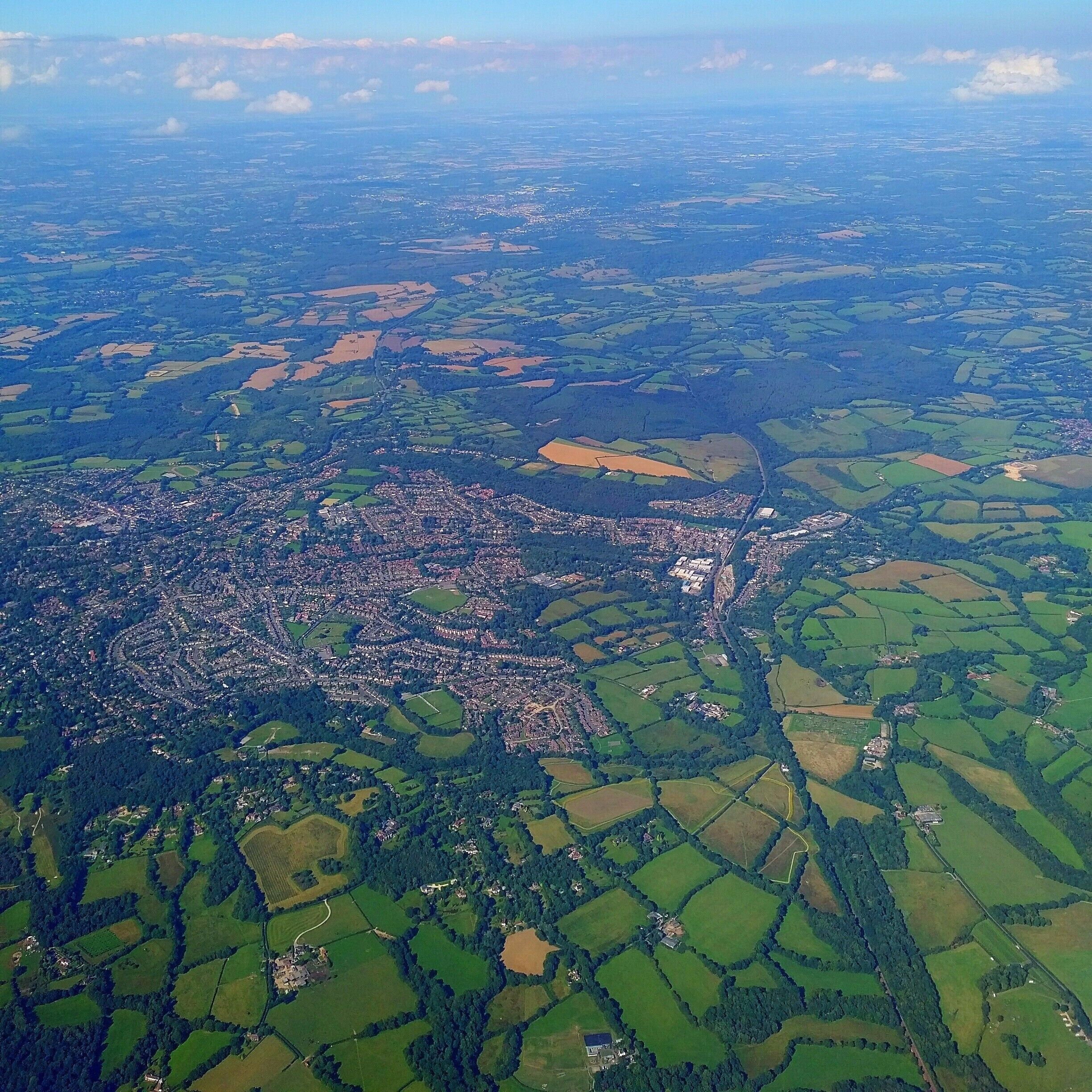 An aerial view of a town surrounded by green fields and patches of farmland.