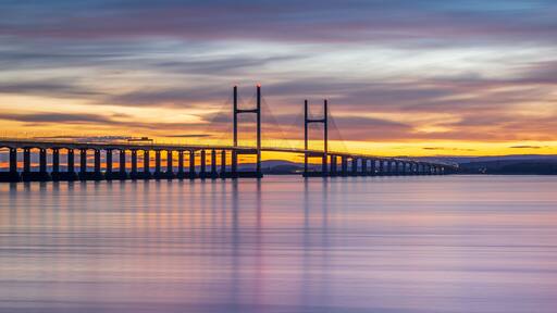 A suspension bridge at sunset with a calm river below.