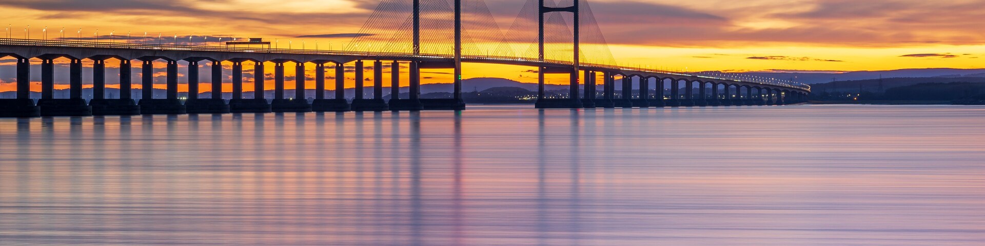 Uma ponte suspensa ao pôr do sol, com um rio calmo abaixo.