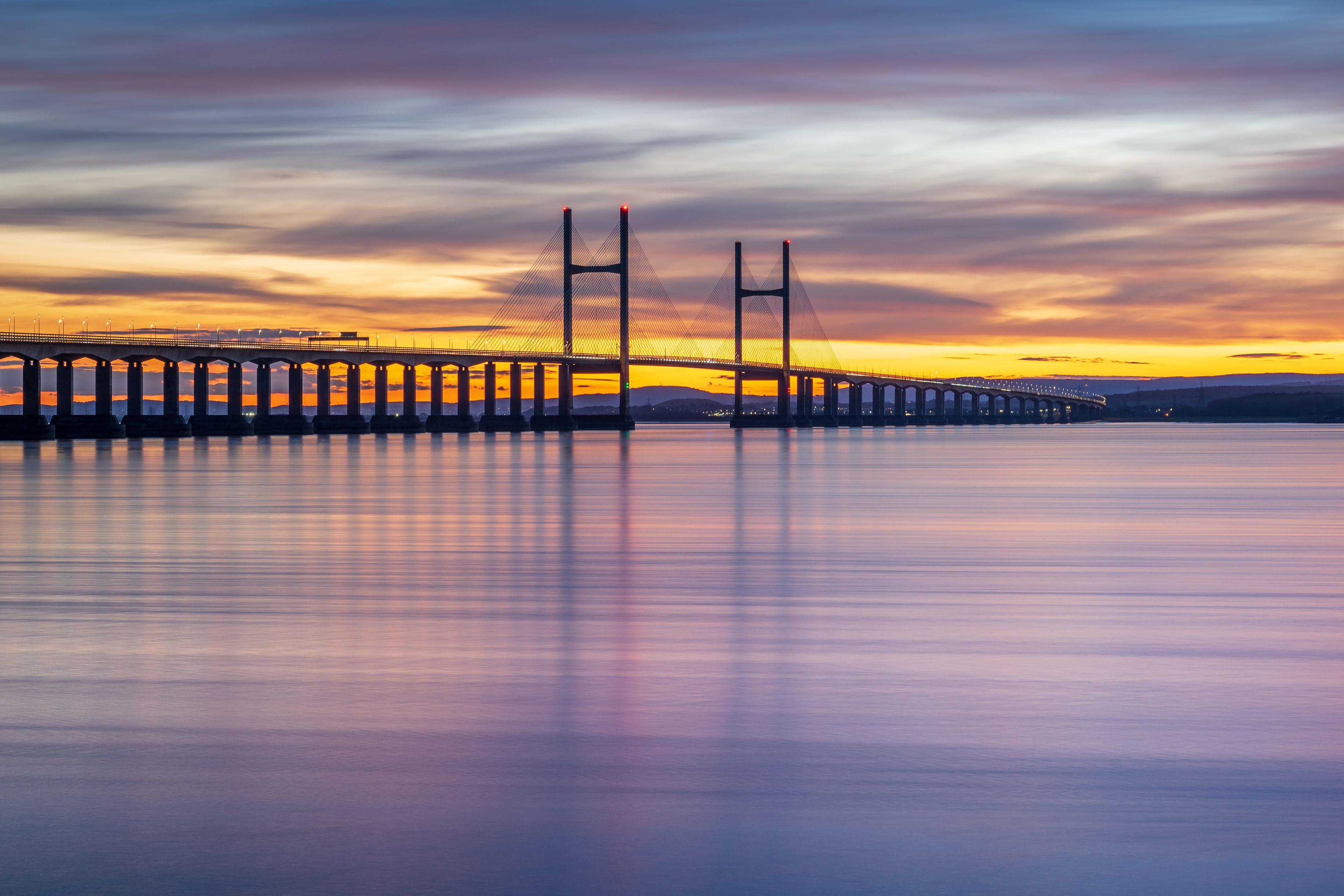 A suspension bridge at sunset with a calm river below.