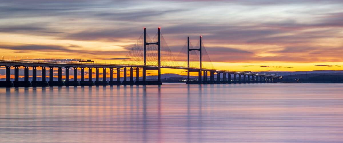 A suspension bridge at sunset with a calm river below.