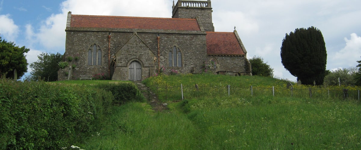 A stone church with a red roof, surrounded by green grass and a large tree.