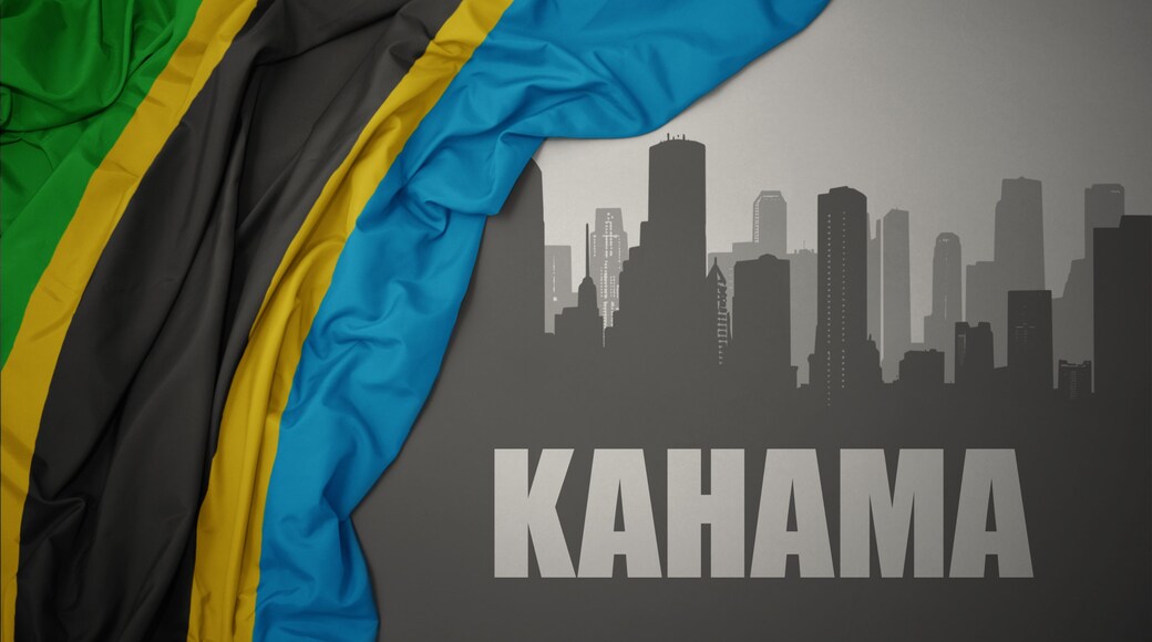 abstract silhouette of the city with text Kahama near waving colorful national flag of tanzania on a gray background.