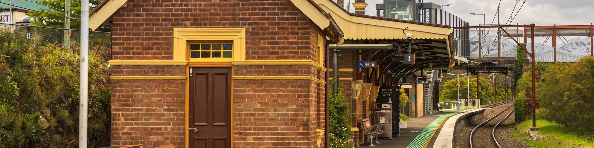 A brick train station with a brown door, a bench, and a platform with a green tactile paving path.