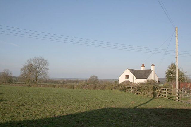 A white house with a red roof, surrounded by a green field and a wooden fence.