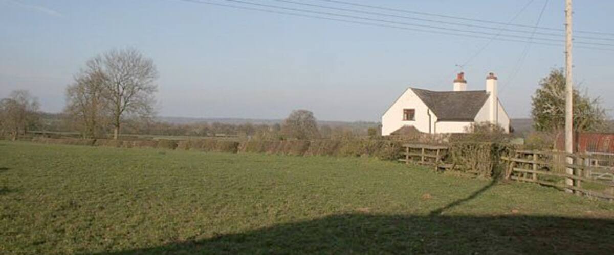 A white house with a red roof, surrounded by a green field and a wooden fence.