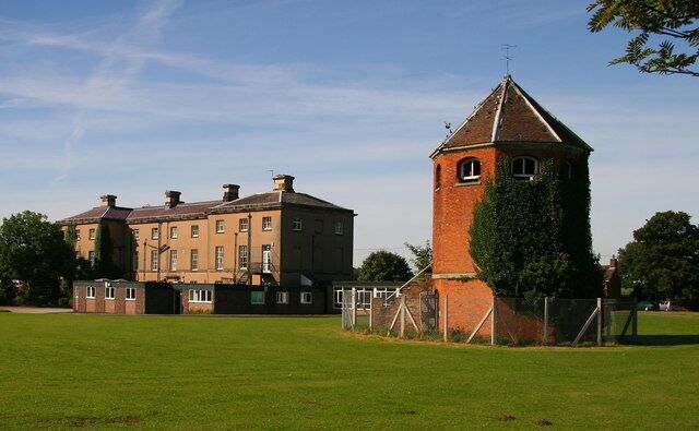 A large brick building with a tower and a grassy field in front.