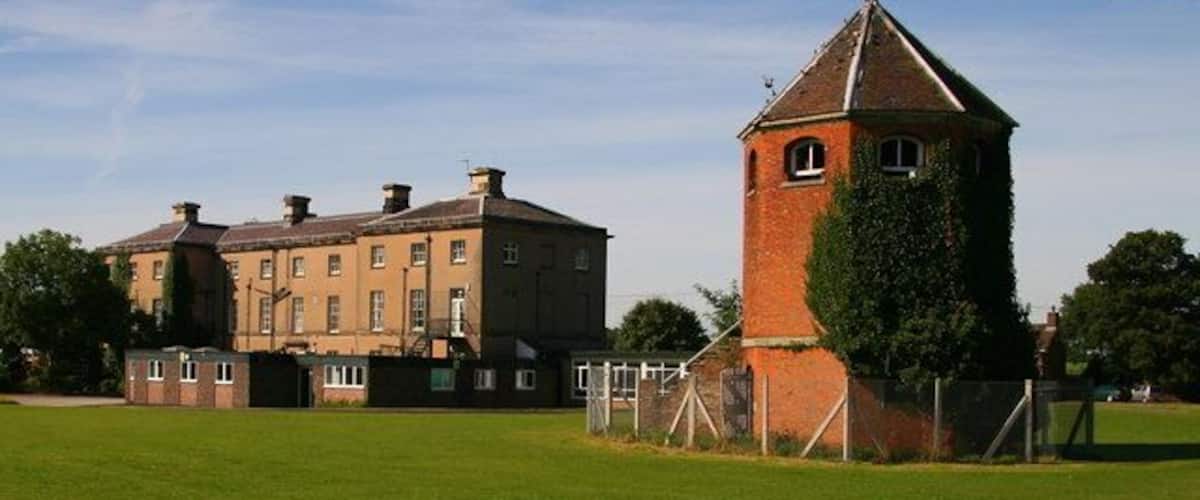 A large brick building with a tower and a grassy field in front.