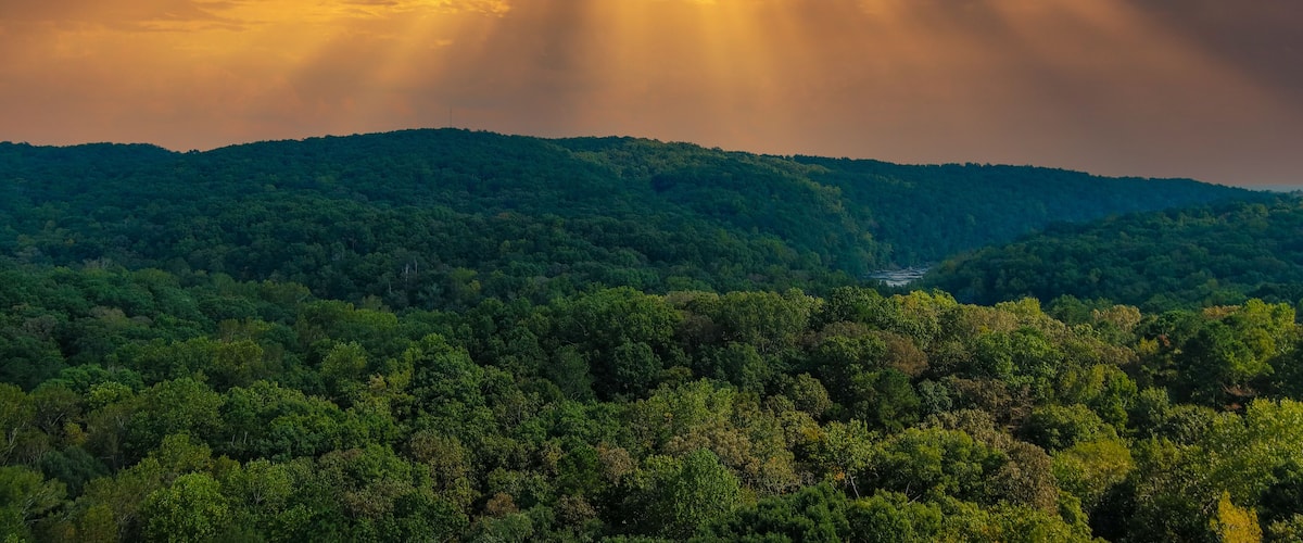 A forested mountain range with sunlight filtering through clouds.