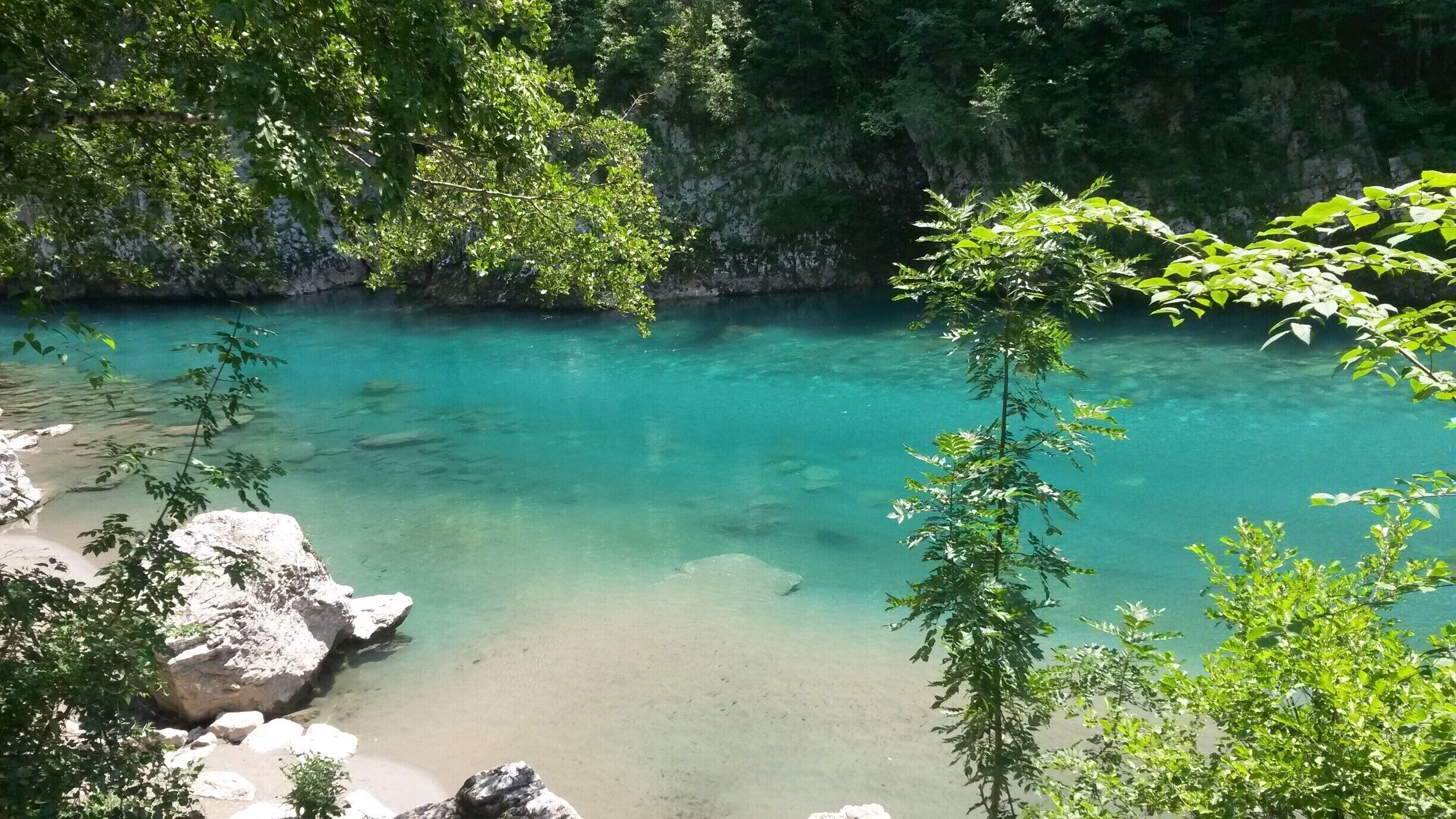 A clear turquoise river surrounded by rocky terrain and lush greenery.