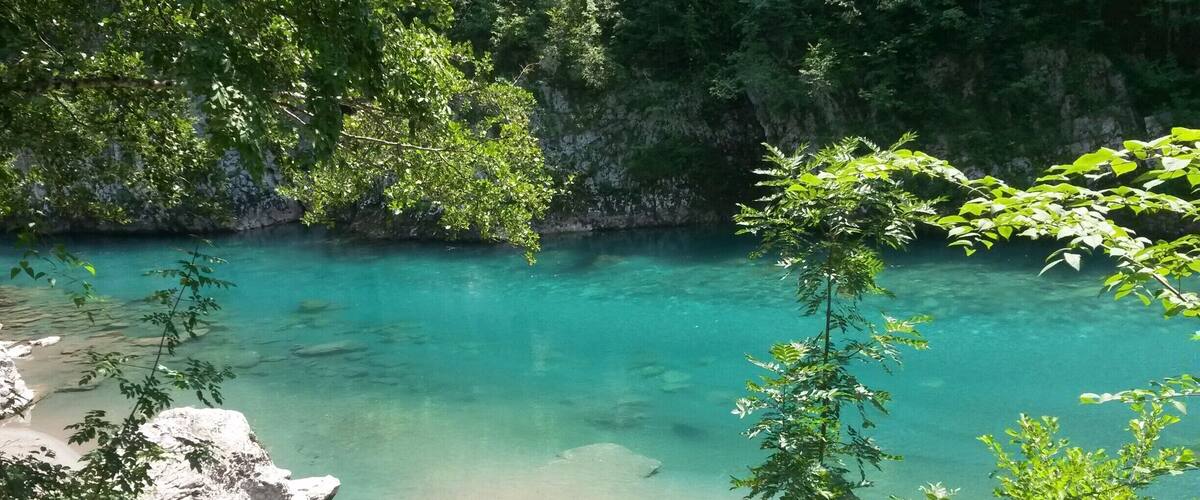A clear turquoise river surrounded by rocky terrain and lush greenery.