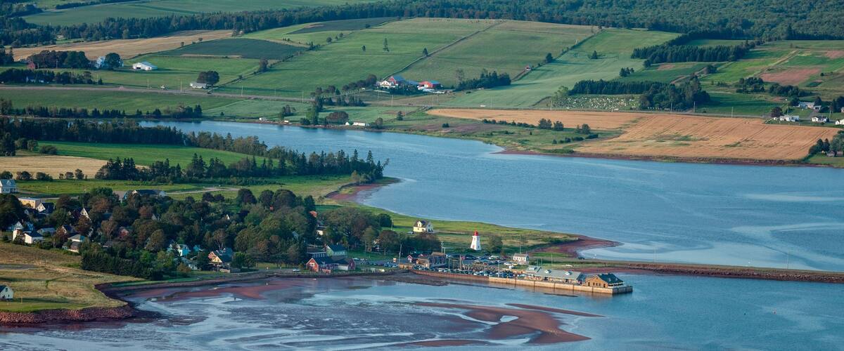 A coastal landscape with a lighthouse, a small harbor, and surrounding fields.
