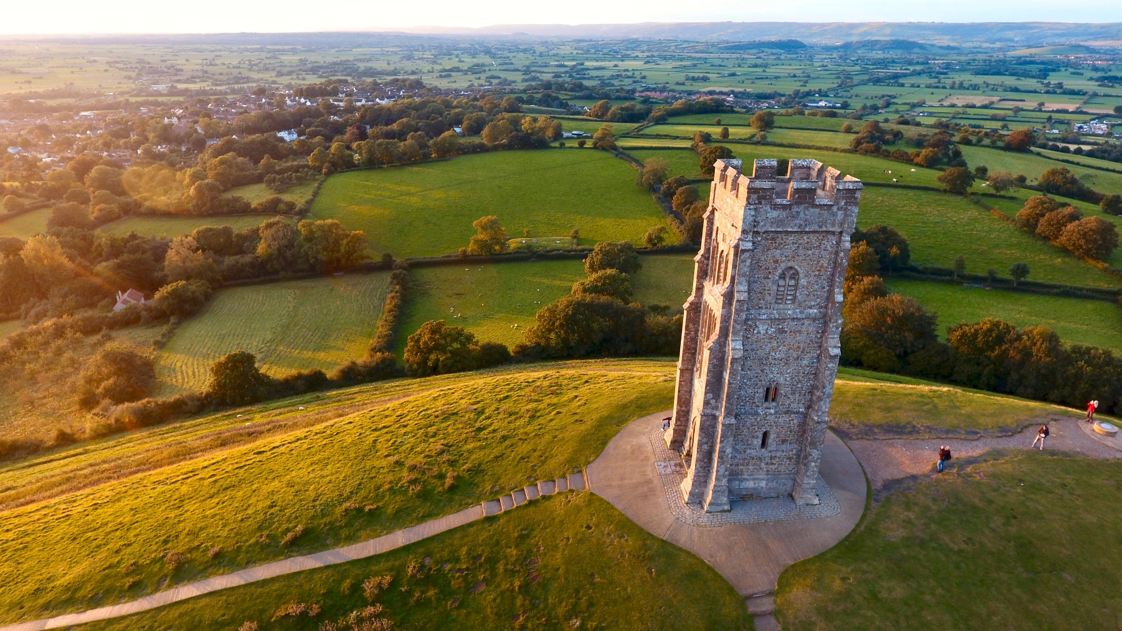 A medieval tower surrounded by rolling green fields and a distant village.