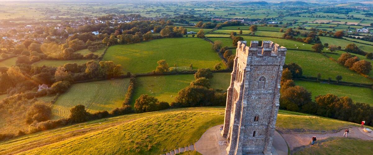 Una torre medieval rodeada de campos verdes ondulantes y un pueblo lejano.