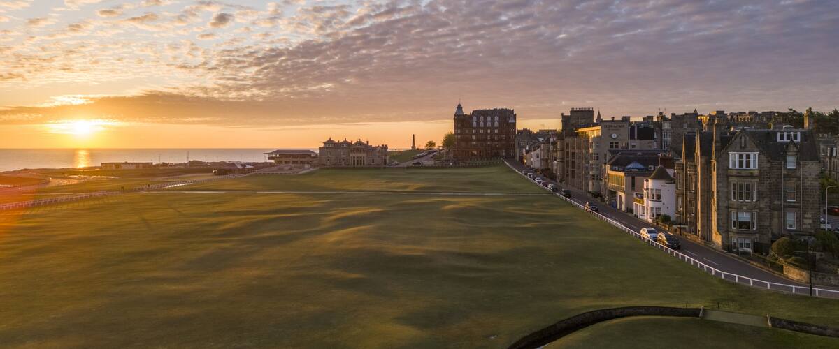 Aerial view of the sun kissing the green expanse of the golf course, blending into the town's edge, with the iconic Hamilton Grand Hotel, St Andrews, Scotland, United Kingdom.